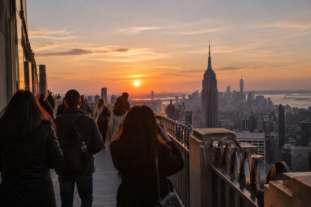 Visitors looking out from the Empire State Building observation deck toward the Manhattan skyline at dusk