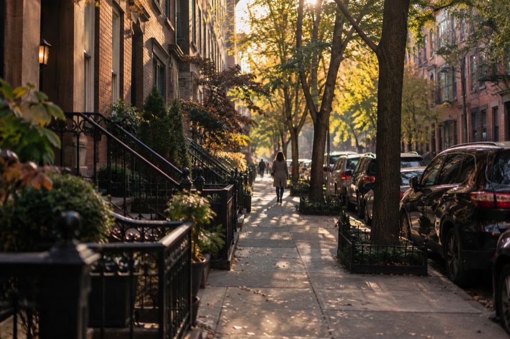 A narrow tree-lined street with brick row houses in Greenwich Village at golden hour