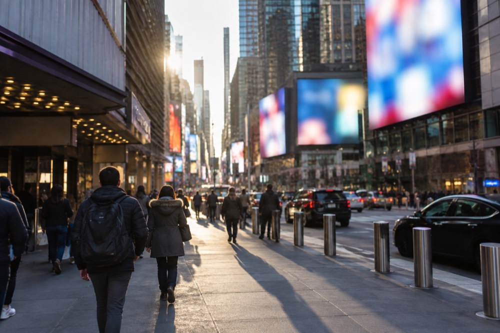 A wide Midtown sidewalk with theater marquees and increasing crowds approaching Times Square