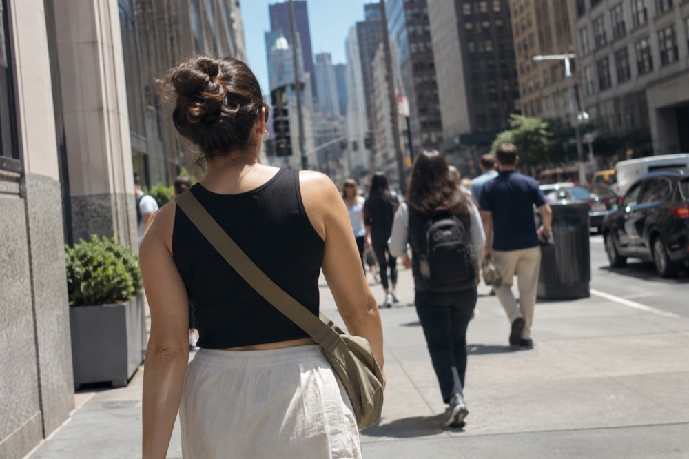 A woman walking a busy Manhattan sidewalk with a crossbody bag