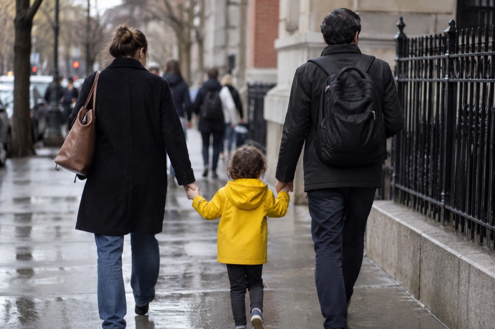 Parents and a small child walking hand in hand on a New York sidewalk near a school entrance