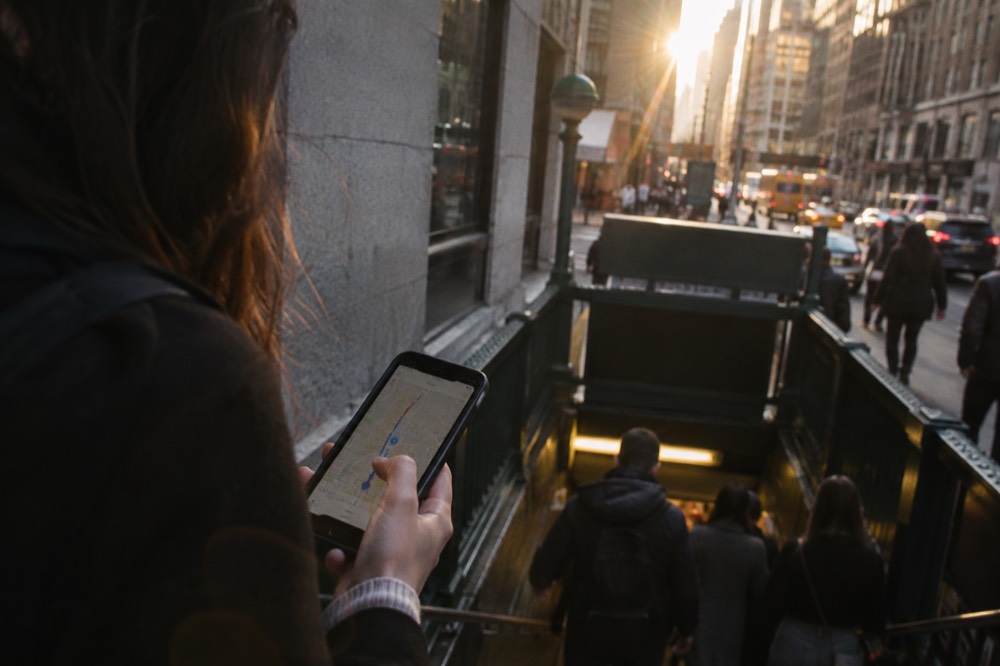 A phone showing a transit route map held above a New York subway entrance