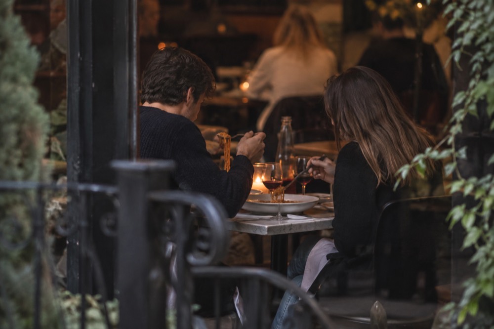 Two people sharing a plate of pasta and wine at a small candlelit table in a Greenwich Village restaurant