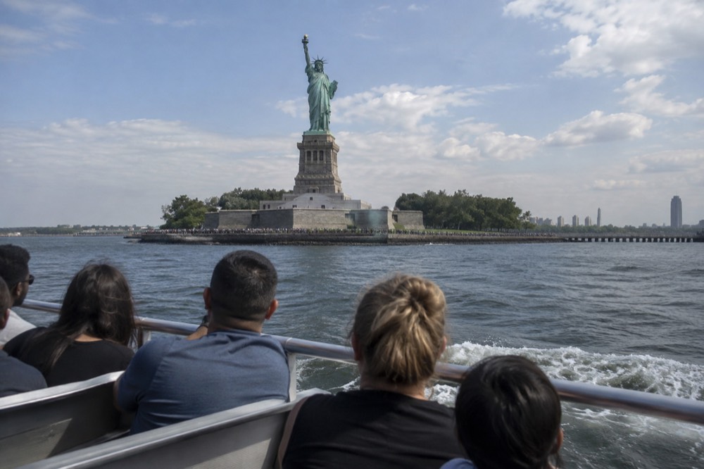 A sightseeing boat passing the Statue of Liberty on a sunny morning in New York Harbor