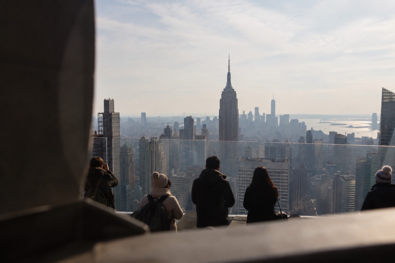 Visitors looking out over the Manhattan skyline from an observation deck on a clear afternoon