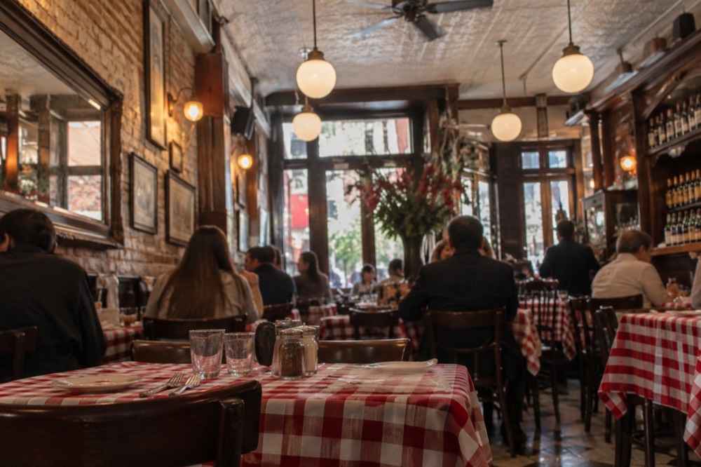 A red-sauce Italian restaurant dining room in Greenwich Village with vintage posters and packed tables