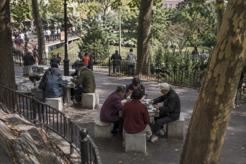 Elderly residents playing mahjong at stone tables in Columbus Park