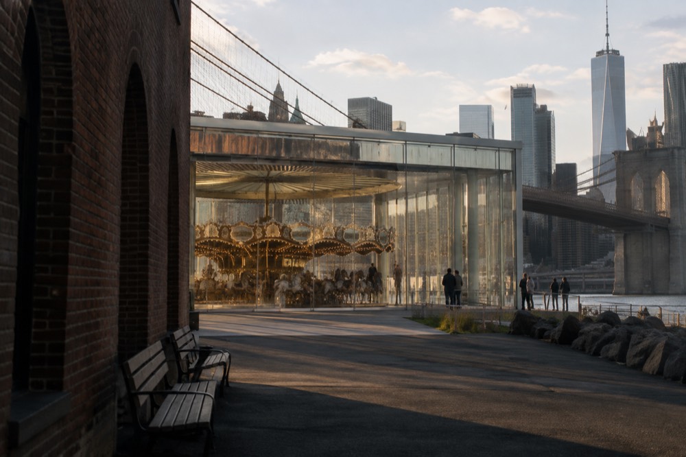 A restored carousel with carved white horses visible through the glass walls of a waterfront pavilion