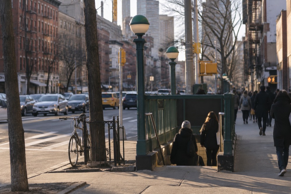 A subway entrance on a busy East Village corner with riders descending the stairs