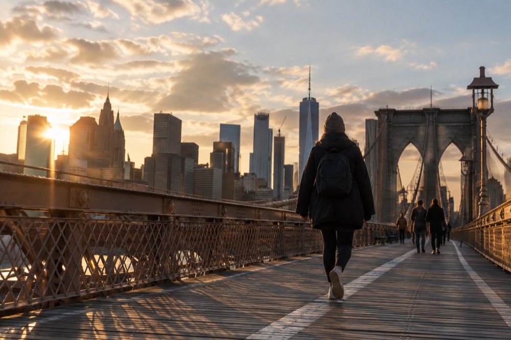 The Brooklyn Bridge promenade at golden hour with Lower Manhattan behind the walker