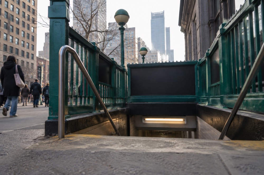A subway entrance with a green railing and sign on a Manhattan sidewalk