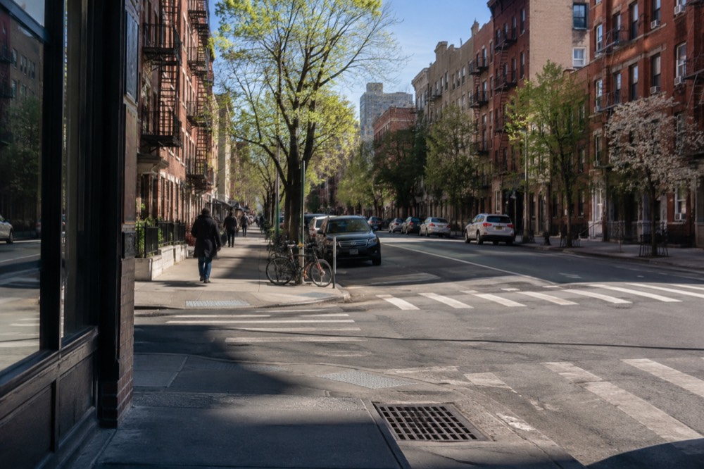 A quiet morning intersection with a crosswalk, parked bikes and brick apartment buildings