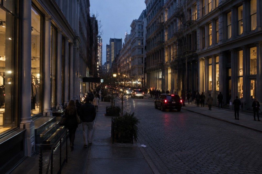 Cast-iron facades and cobblestone street in SoHo with shoppers walking past storefronts