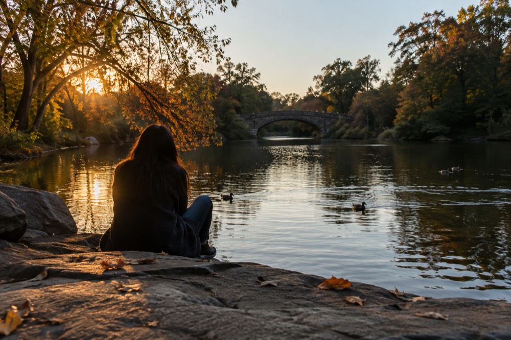 The Prospect Park lake with tree-lined shores and a stone arch bridge in the distance