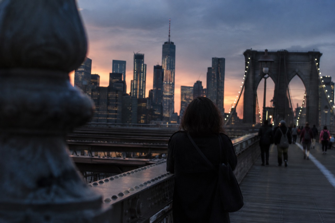 The Brooklyn Bridge promenade with the Manhattan skyline rising behind it at golden hour