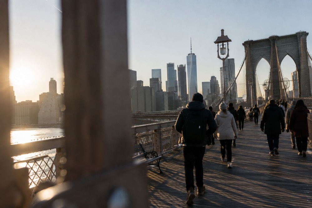 Pedestrians crossing the Brooklyn Bridge promenade with the skyline behind them