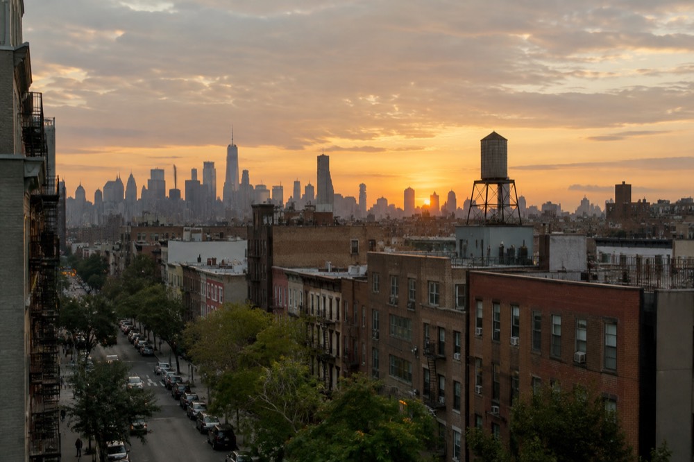 Row of low brick buildings and a water tower against a Brooklyn skyline at golden hour