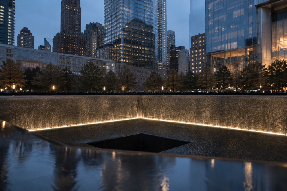 Water falling into the center void of a memorial pool at dusk, lit from below