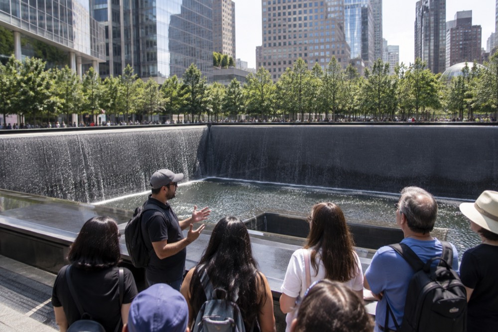 A guide speaking to a small group of visitors beside the memorial pools on a Financial District walking tour