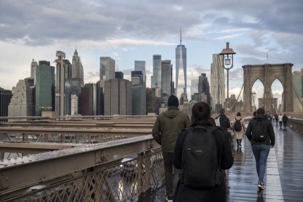 Walkers on the Brooklyn Bridge promenade with the Manhattan skyline ahead across the East River