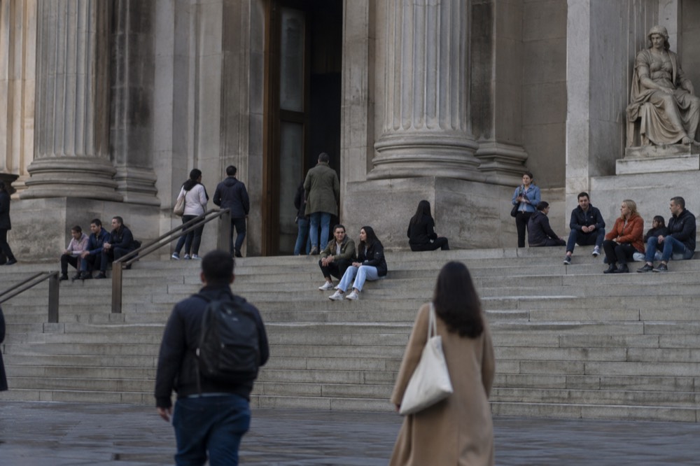 People relaxing on the wide stone steps outside a large museum building in Brooklyn