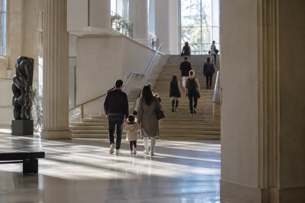 A family walking through a bright museum atrium toward a stairway