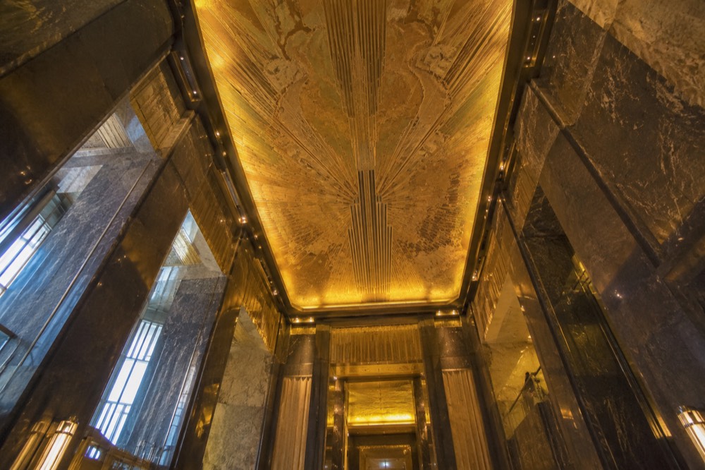 Looking up at the Art Deco lobby ceiling of the Empire State Building, gilded and lit