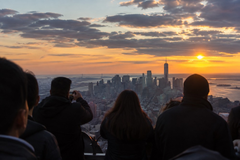 Visitors on a crowded observation deck at sunset, silhouetted against the glowing skyline