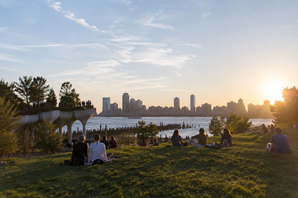 People relaxing on a grassy lawn on an elevated park with the Hudson River behind them