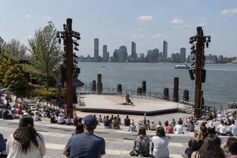 An outdoor amphitheater with tiered stone seating facing an open stage and the river beyond