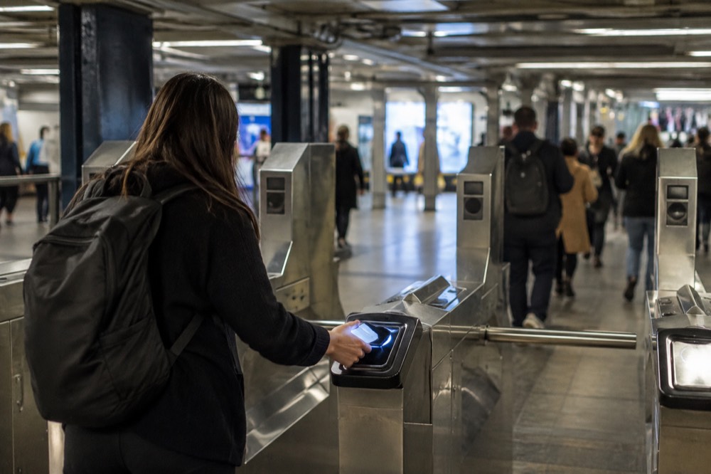A traveler tapping a phone at a subway turnstile inside a New York station