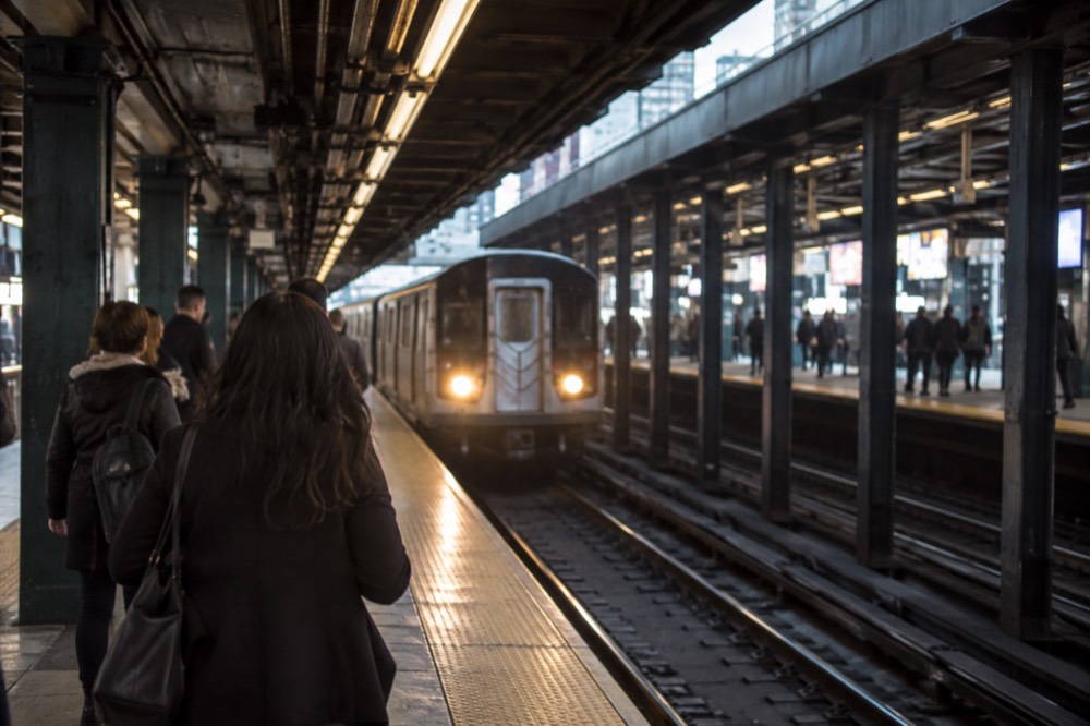 A subway platform in Midtown Manhattan with a train arriving and passengers waiting