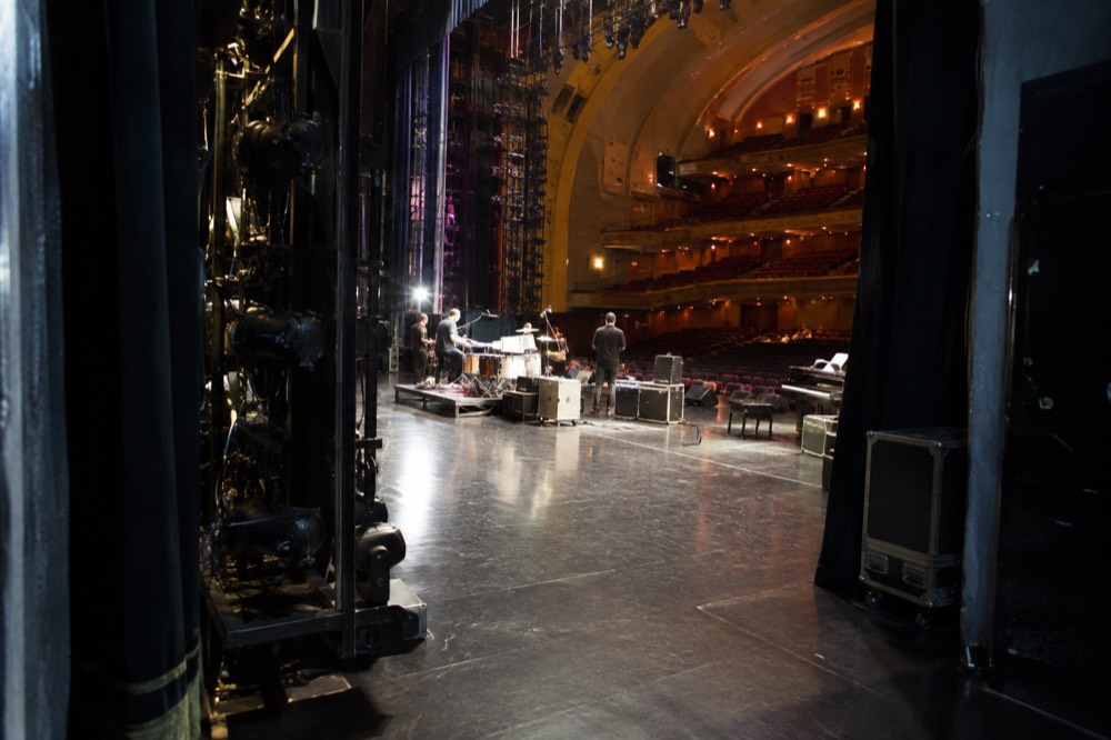 The stage of a large theater seen from the wings with stage lighting rigging visible