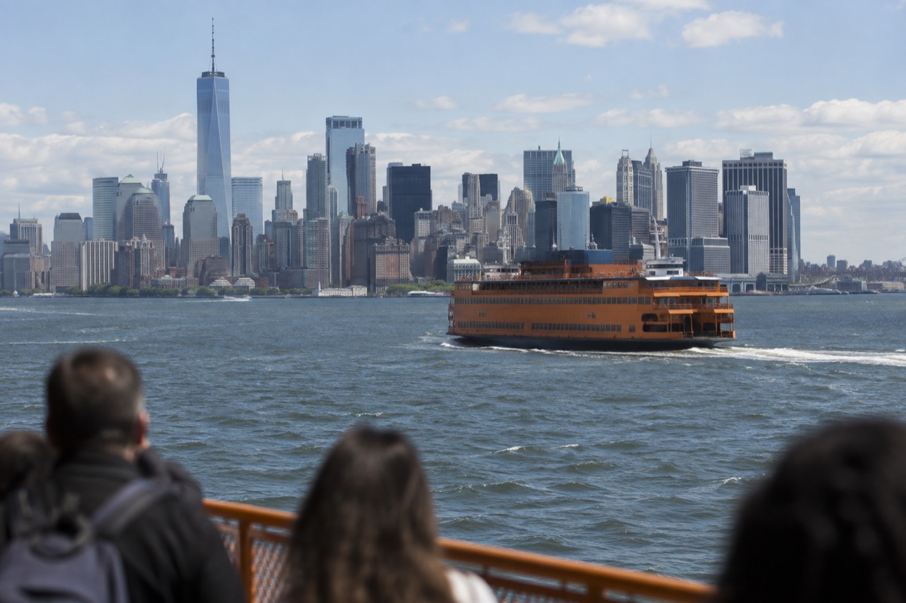 An orange Staten Island Ferry boat crossing New York Harbor with the Lower Manhattan skyline behind it