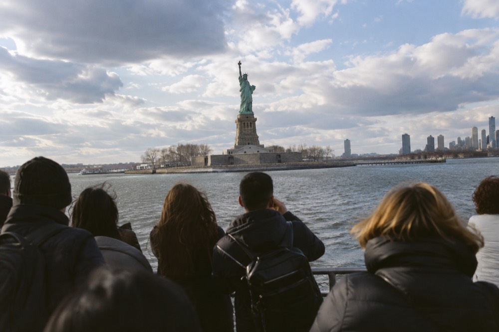 Ferry passengers at the railing approaching the Statue of Liberty across New York Harbor