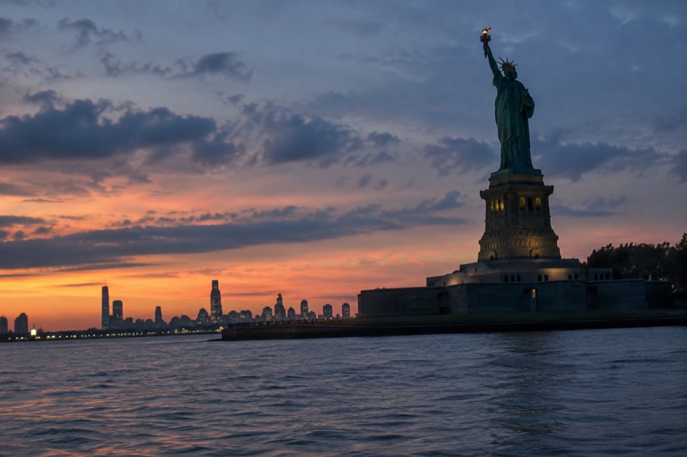 The Statue of Liberty seen from the water at sunset with the torch lit