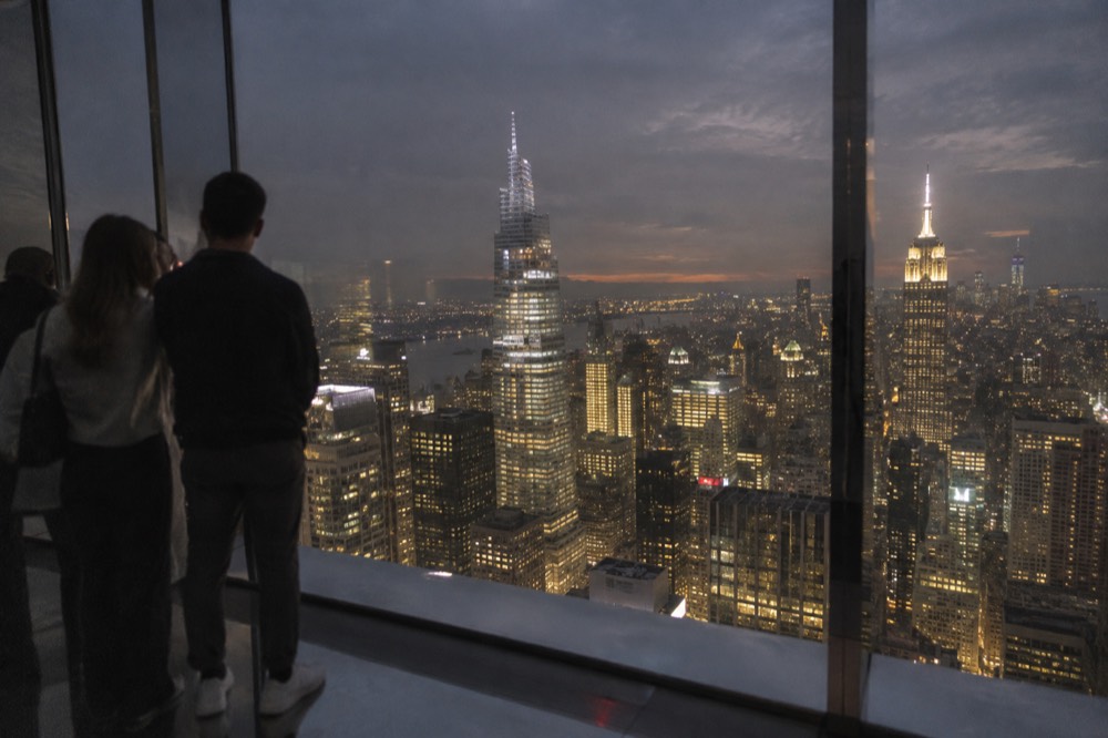 A city skyline at night with illuminated towers seen from high above through a large glass window