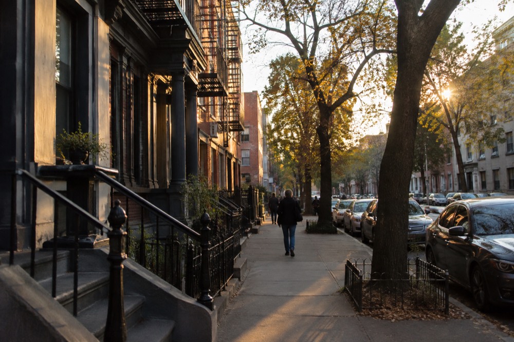 A quiet residential street of old low-rise apartment buildings in late afternoon light