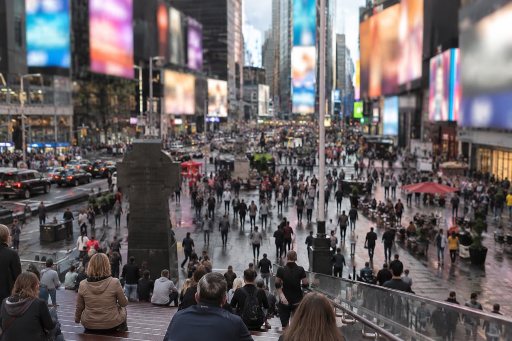 Pedestrians filling the Times Square plaza on a sunny afternoon with billboards overhead