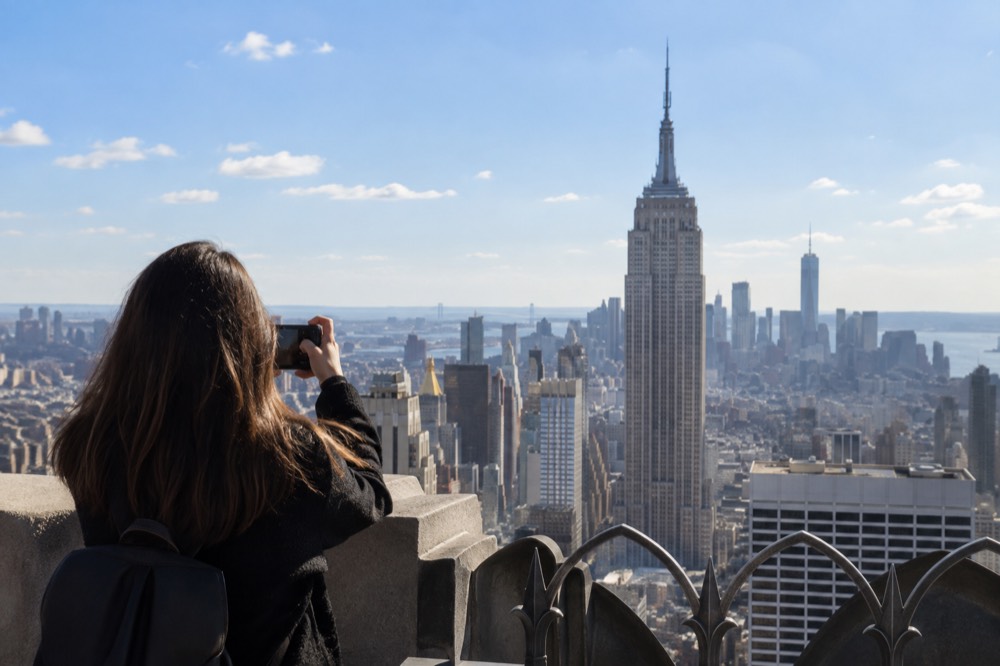A visitor photographing the Empire State Building from the open-air 70th floor of Top of the Rock