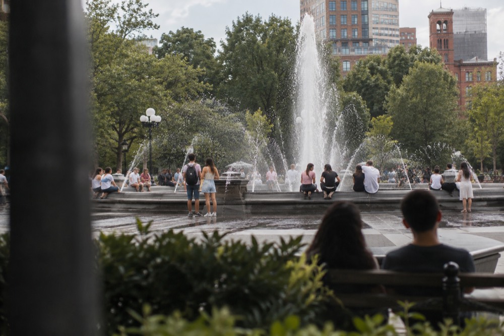 People gathered around the central fountain in Washington Square Park on a warm day