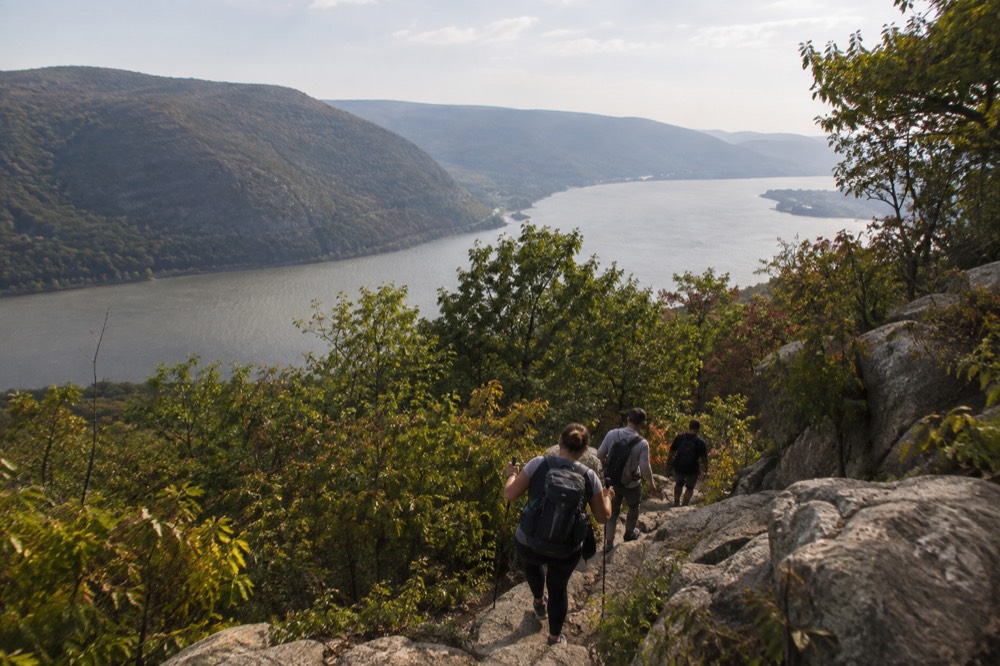 Hikers climbing a rocky ridge trail above the Hudson River