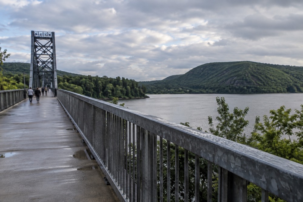 A long elevated pedestrian bridge stretching across a wide river between wooded banks