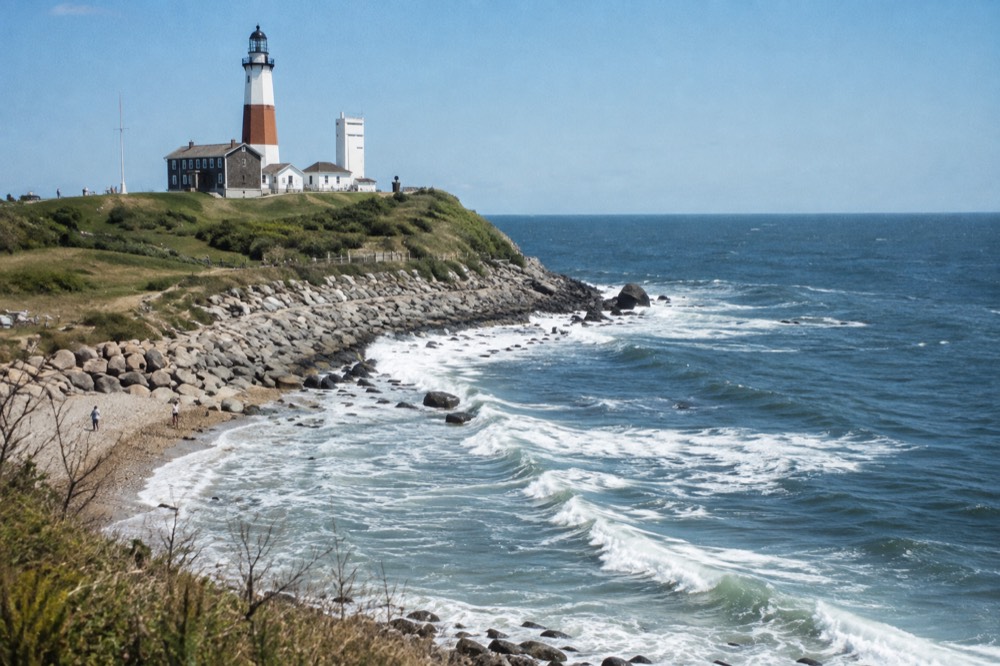 A white lighthouse with a red stripe above rocky shoreline and breaking waves
