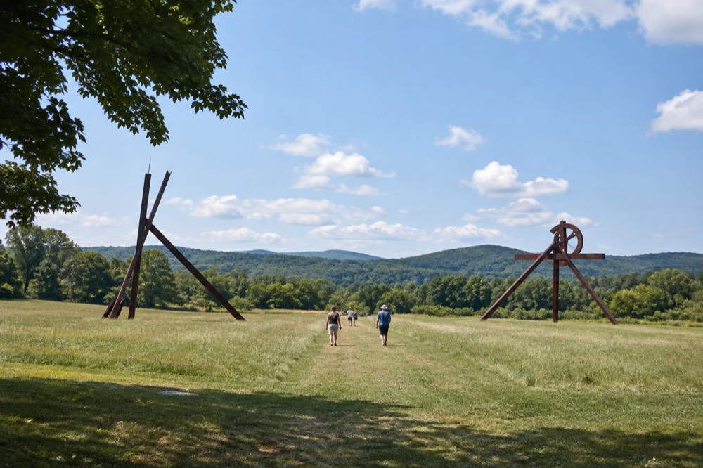 Visitors walking a long mown path between two large metal sculptures under a wide sky