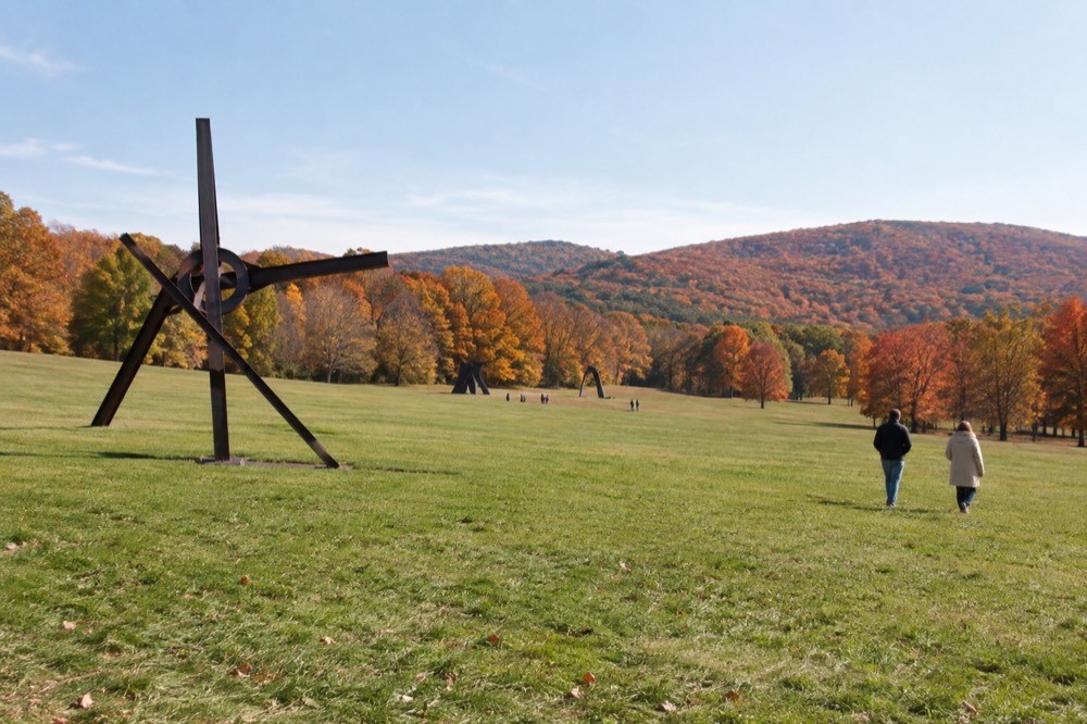 Hillsides covered in orange and red autumn trees behind a field of sculpture
