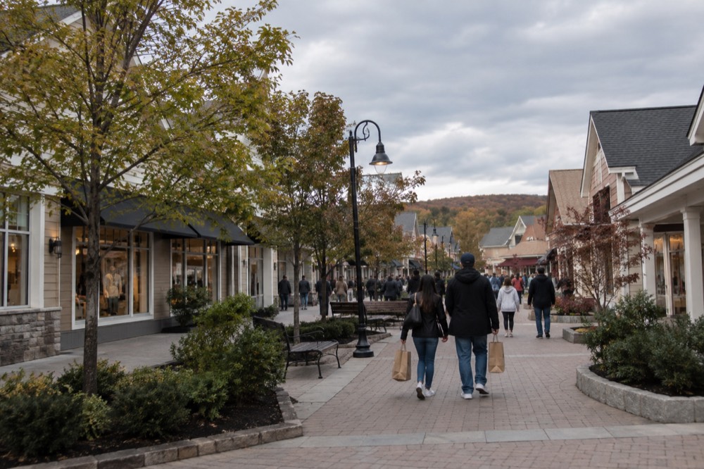 Wide view of an outdoor outlet shopping center with tree-lined walkways between stores