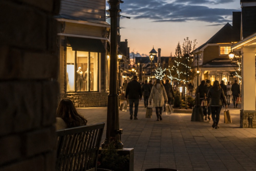 Evening view of an outlet village walkway lit by storefront lights after dark