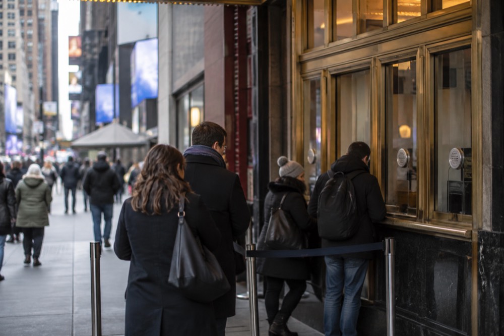 A theater box office window in Midtown Manhattan with the playbill posters lit behind the glass