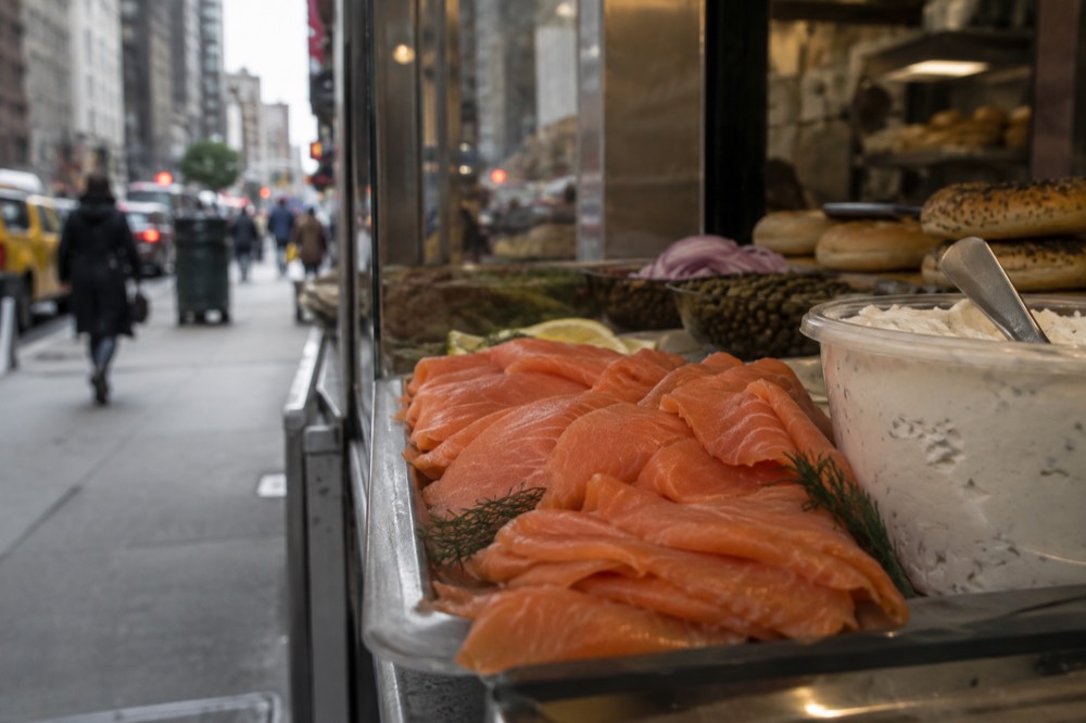 Slices of smoked salmon arranged on a deli counter next to a tub of cream cheese